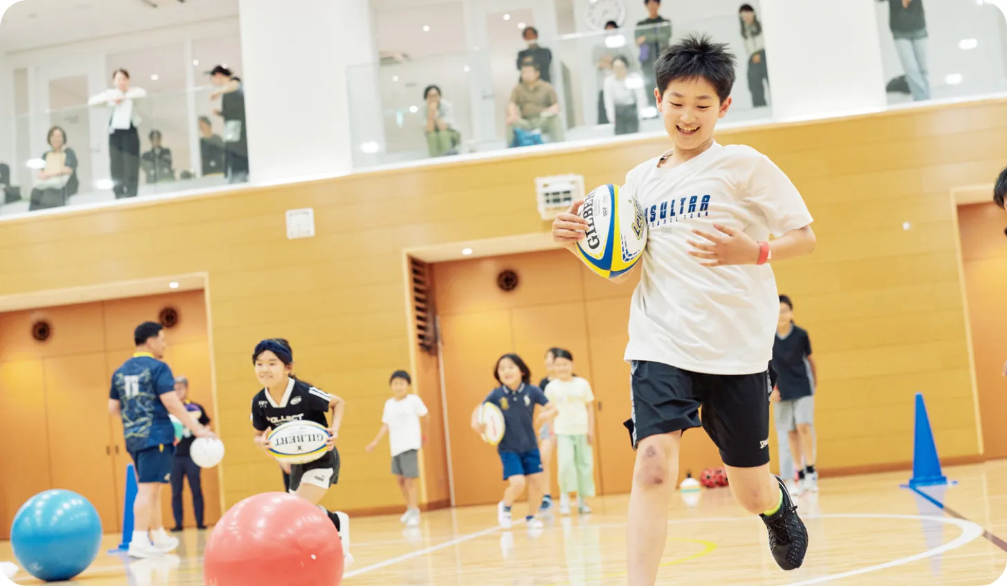 ラグビーボールを持って走る子ども